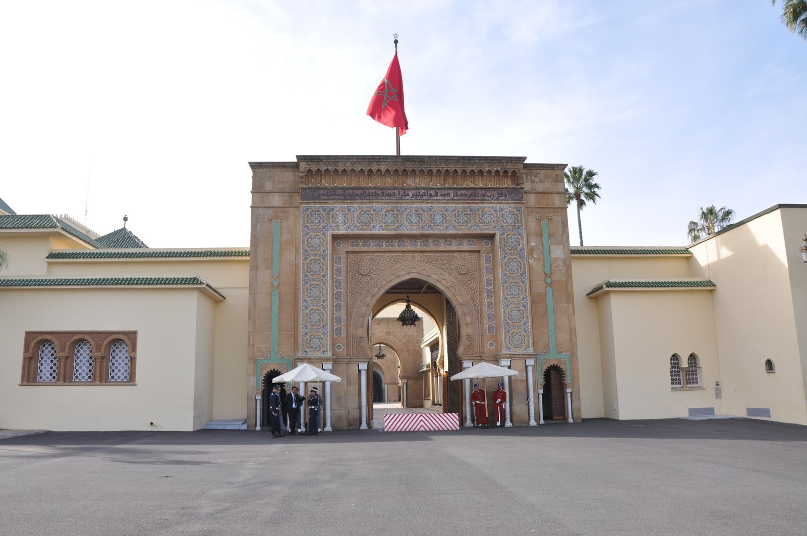 Porte monumentale du palais royal de Rabat, ornée de zelliges et surmontée du drapeau marocain, avec des gardes à l'entrée