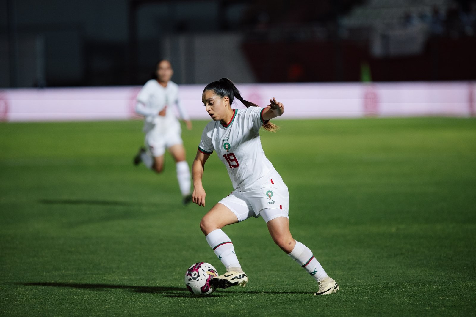 Sakina Ouzraoui Diki, en maillot blanc du Maroc, conduisant le ballon sur la pelouse