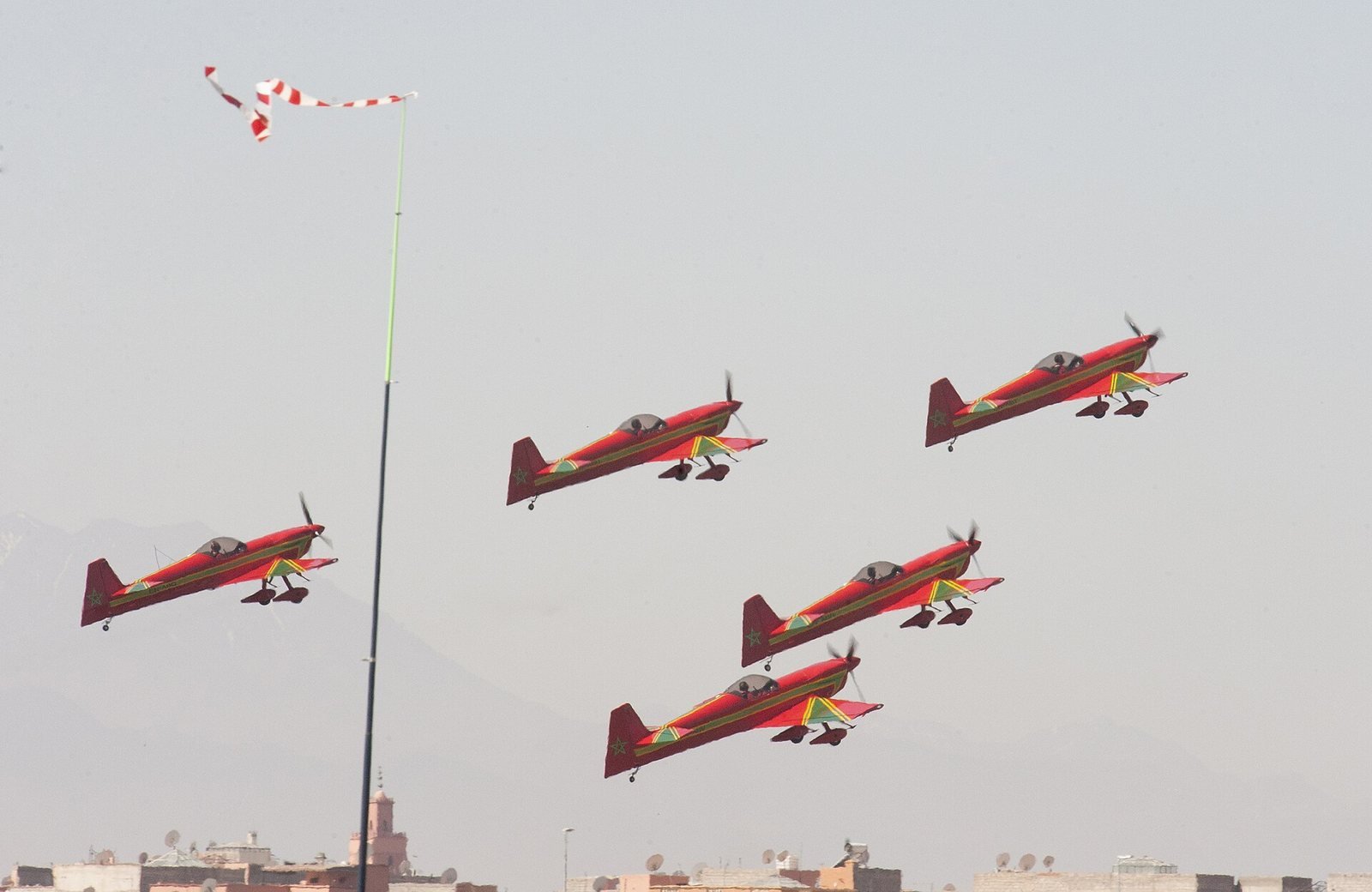 Cinq avions de voltige rouges de la patrouille Marche Verte volant en formation au-dessus des toits de Marrakech, une manche à air rouge et blanche au premier plan