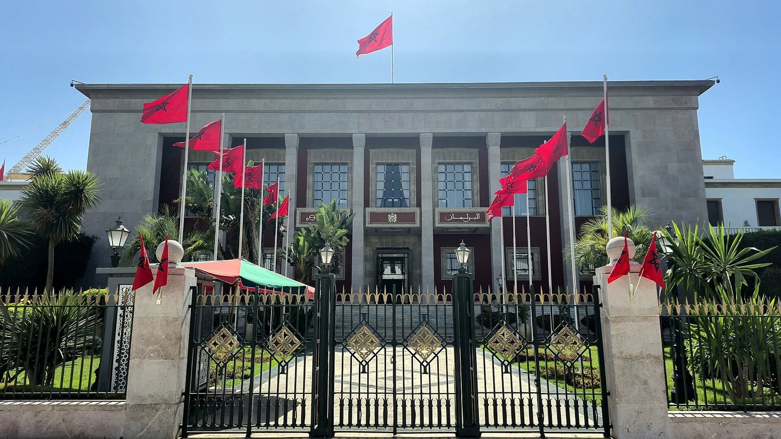 Façade du siège du Parlement à Rabat, ornée de drapeaux marocains, derrière sa grille d'entrée